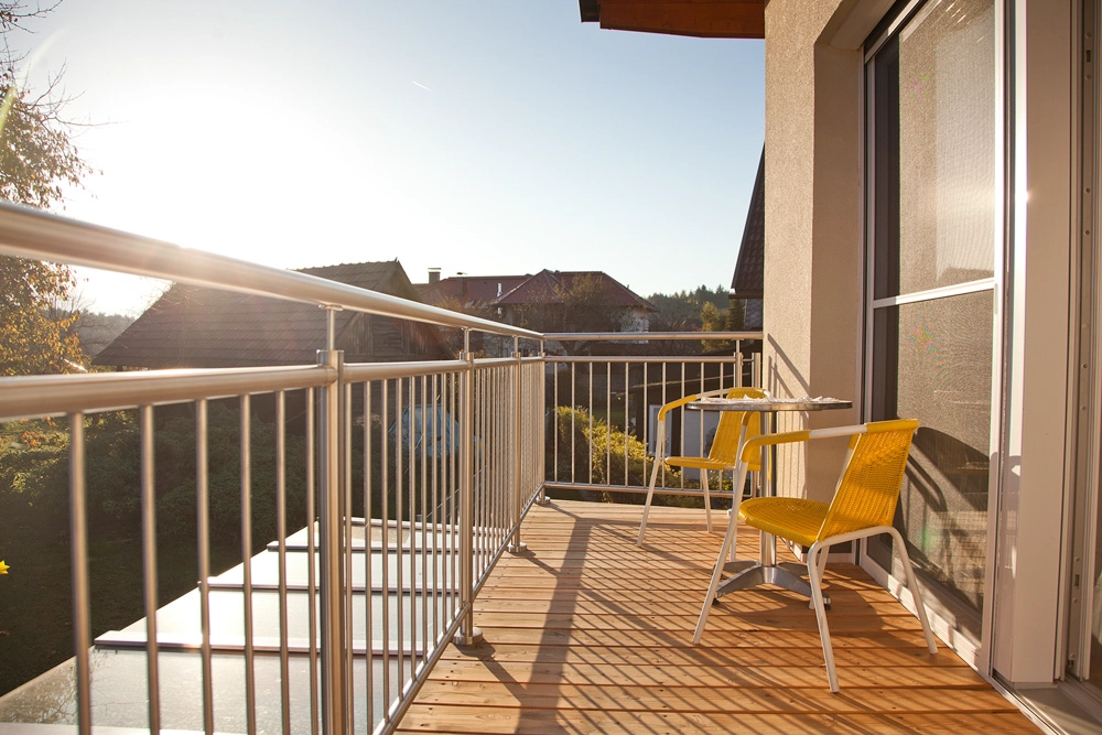 Ferienwohnung Greiler – Außenansicht eines Balkones einer Immobilie in Kärnten auf einem Balkon mit Tisch und gelben Stühlen, Sonnenschein und lieblichen Ambiente.